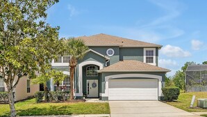 A two-story house with a garage, a front yard, and a palm tree. - Emerald Island Resort 6 Bed Pool & Spa-10min to Disney! (Kissimmee)