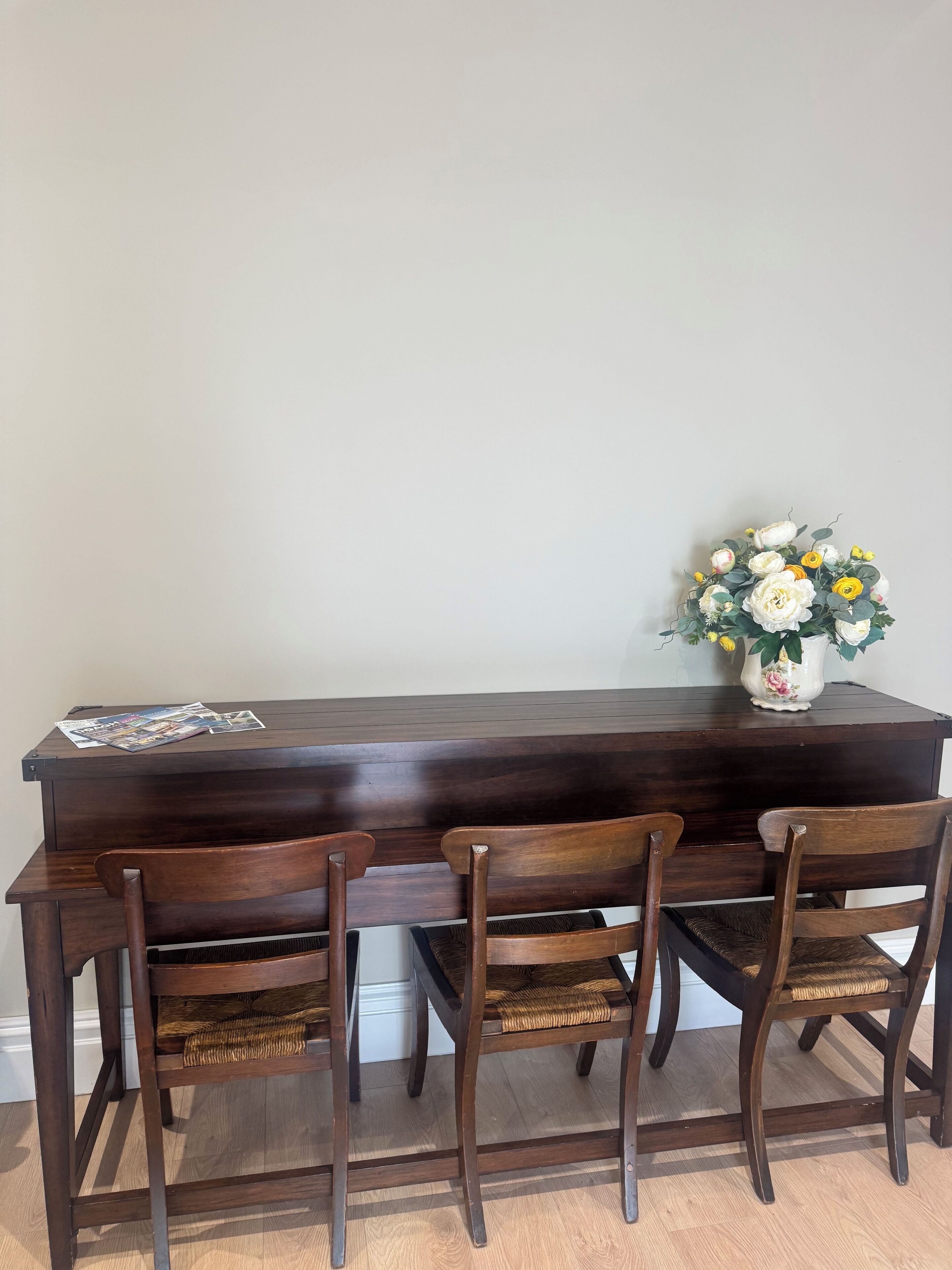 Une table de salle à manger en bois foncé, avec quatre chaises, un vase rempli de fleurs et un magazine posé sur la table.