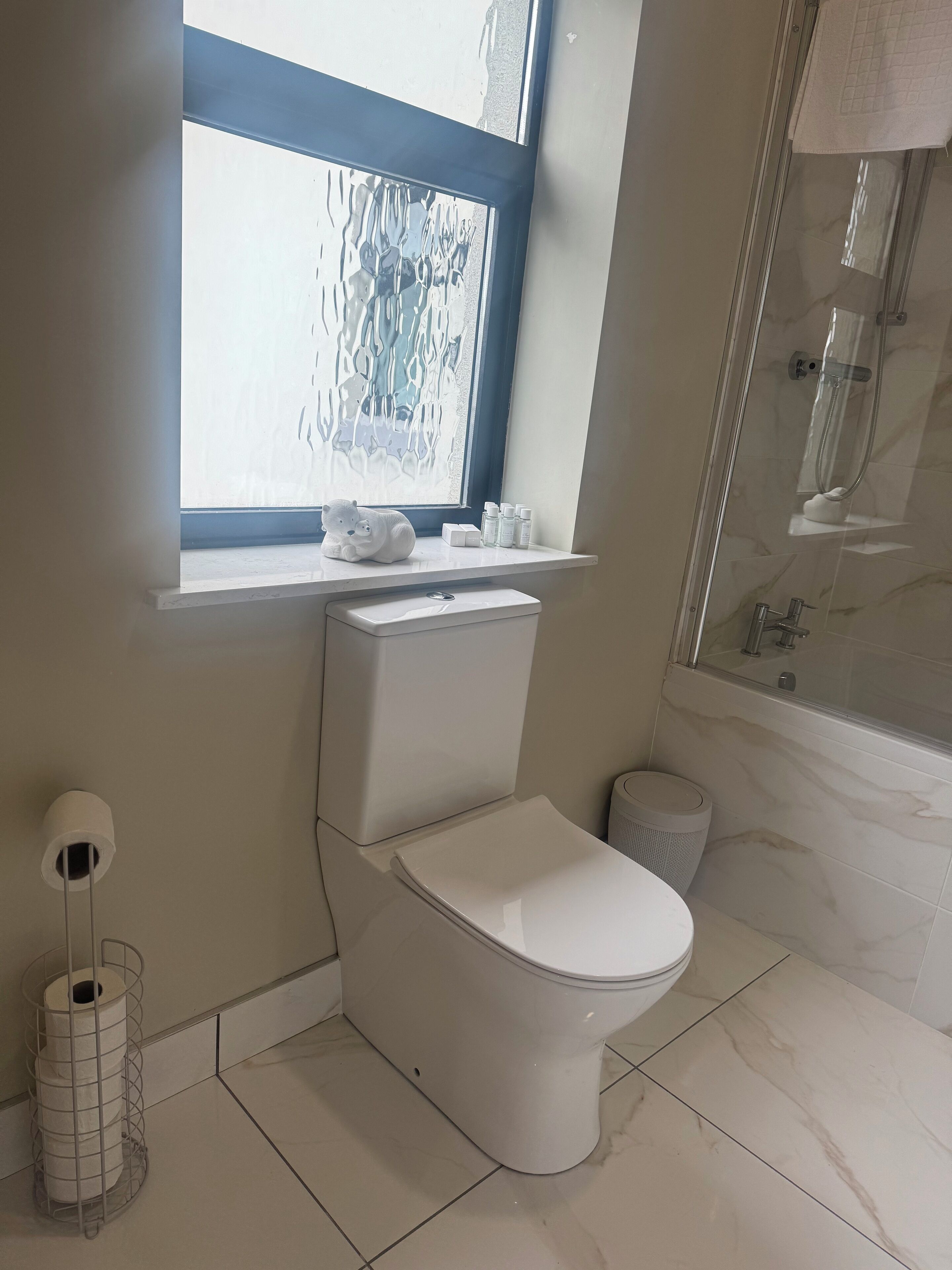 A modern bathroom with a toilet, a window, and a shower area.