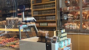 Un comptoir de produits de charcuterie proposant diverses viandes emballées et autres produits de charcuterie, une caisse enregistreuse et un présentoir de condiments.
