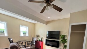 Una sala de estar con ventilador de techo, televisor, sofá, mesa de comedor con sillas y una planta en maceta.