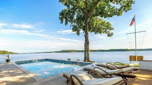 A pool area with lounge chairs, a flag, and a view of a lake. - Panoramic Paradise - Lakefront Home for 15 (Rocky Mount)