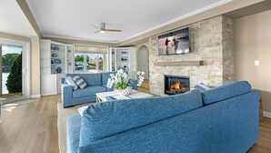 A modern living room with a stone fireplace, blue sofas, and a TV mounted on the wall. - Panoramic Paradise - Lakefront Home for 15 (Rocky Mount)