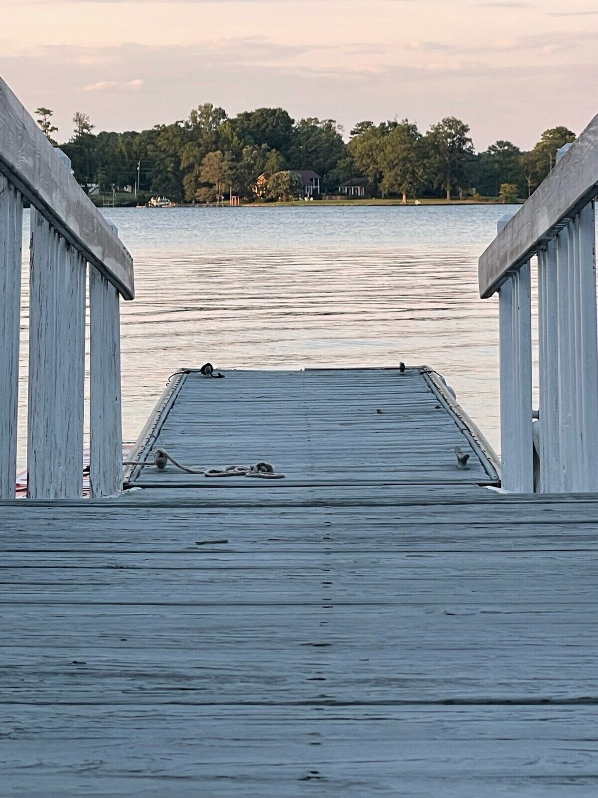 A wooden pier extending into calm water with a view of a forested shoreline in the distance.