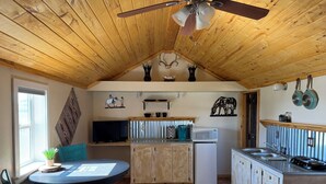 Una cocina acogedora con techo de madera, una mesa de comedor con sillas, un televisor y un microondas.
