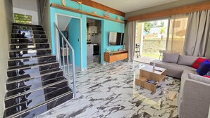 A spacious living area with a marble floor, a staircase, a sofa, and a television.
