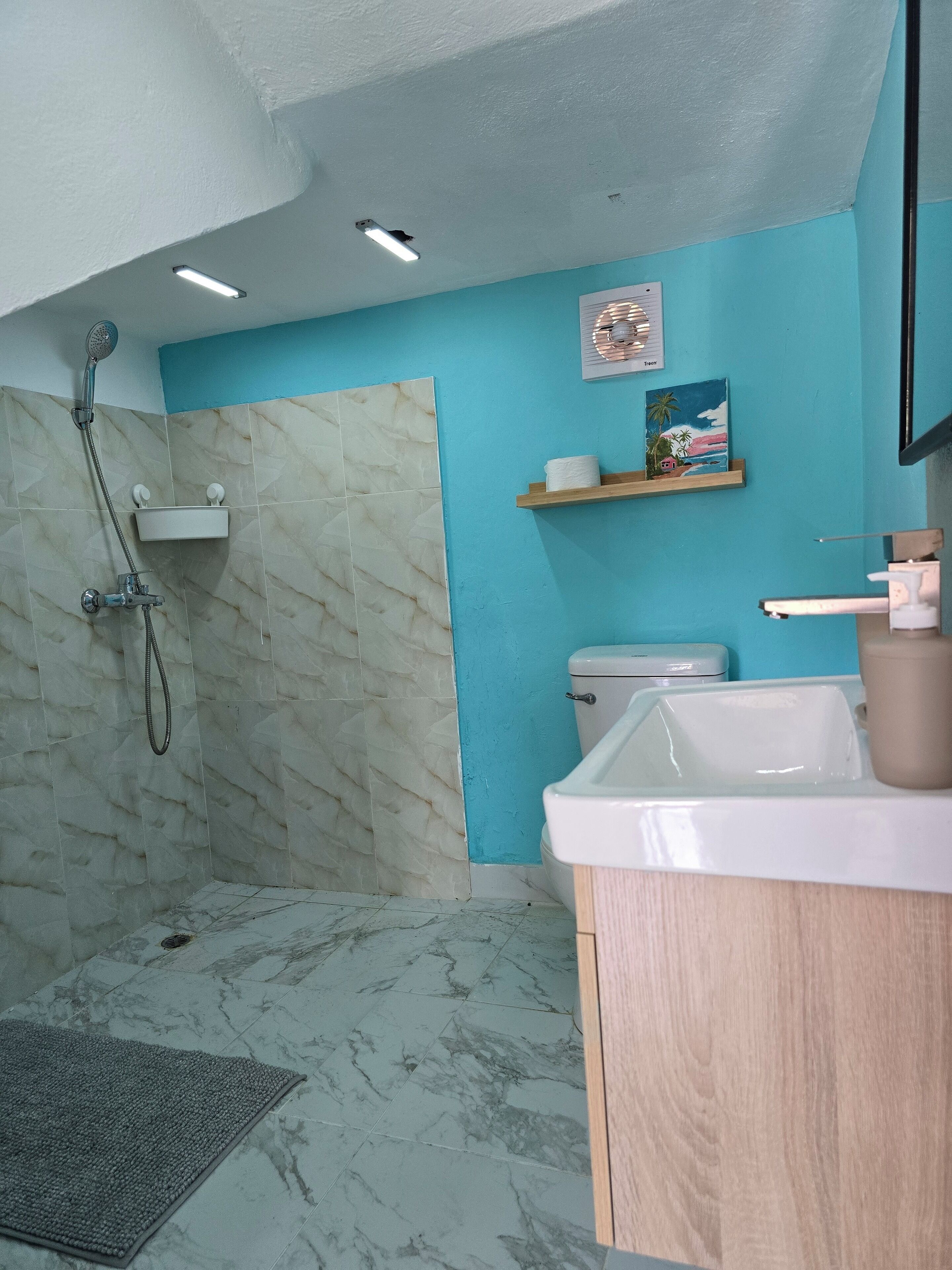 A bathroom with a shower, toilet, sink, and marble flooring.