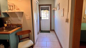 A narrow hallway with a kitchen area on the left, a door at the end, and a small seating area with a chair. - Pet Friendly Guesthouse Near the Beach/Downtown (Melbourne)