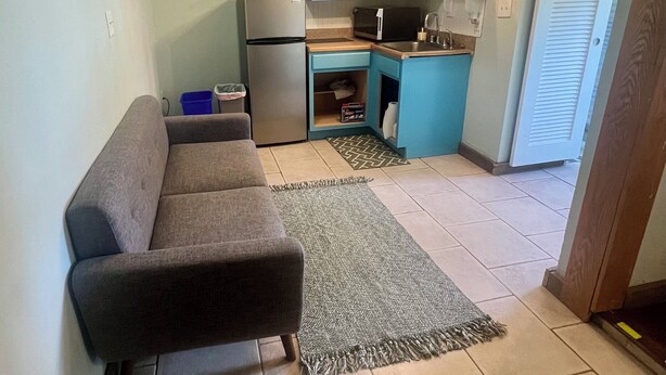 A compact kitchen with a refrigerator, microwave, and sink. There's a sofa and a patterned rug in the living area. - Pet Friendly Guesthouse Near the Beach/Downtown (Melbourne)