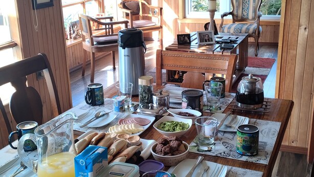 A dining area with a wooden table set for breakfast, including bread, eggs, and beverages. - Double room in a family home (Dalcahue)