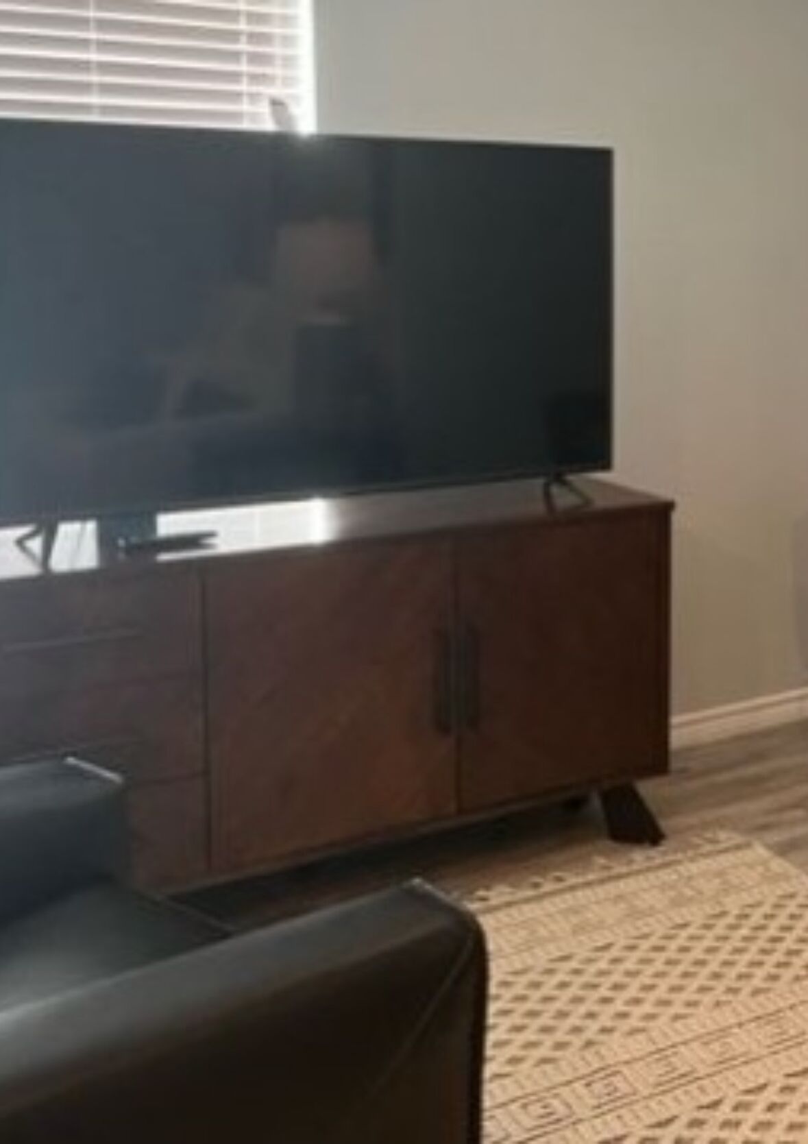 Ein Wohnzimmer mit einem Flachbildfernseher auf einer Holzeinrichtung, einem braunen Ledersofa und einem gemusterten Teppich.