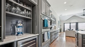 A modern kitchen with built-in appliances, a dining area with a large window, and a cozy seating area. - Luxury 4BR Smart Home w/ Pool, Spa, Media Room & Pet-Friendly Yard (Frisco)