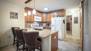A kitchen with wooden cabinets, a granite countertop, a white refrigerator, and pendant lights. - Waterwheel Hideaway - Cozy Condo for 6 With Resort-style Amenities (New Braunfels)