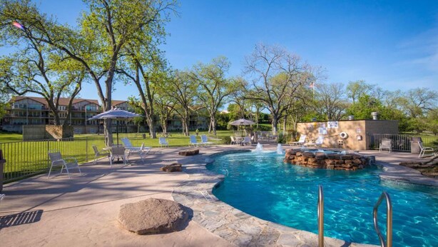 A swimming pool with lounge chairs and a hot tub, surrounded by trees and a fence. - Waterwheel Hideaway - Cozy Condo for 6 With Resort-style Amenities (New Braunfels)