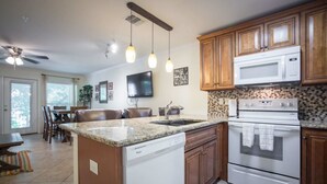 A kitchen with granite countertops, wooden cabinets, a dishwasher, a microwave, and an oven. - Waterwheel Hideaway - Cozy Condo for 6 With Resort-style Amenities (New Braunfels)