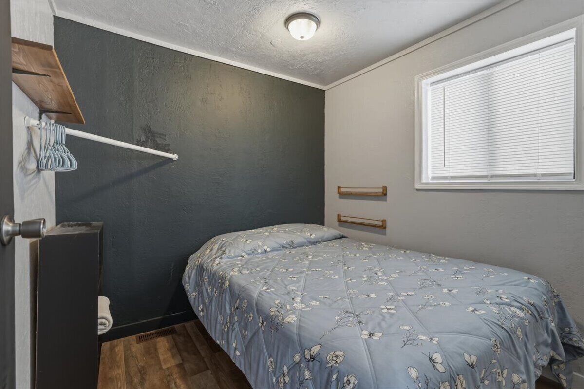 Une petite chambre à coucher, de taille réduite, avec un lit simple, une fenêtre avec des stores, un porte-serviettes et une porte.