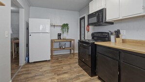 A compact kitchen with white cabinets, a black stove, a microwave, and a wooden countertop. - 10mins to Air force base|Smart TV|Self Check-In (Mountain Home)