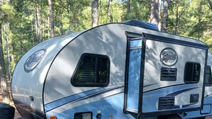 A silver RV with a side door, a small window, and a logo on the side.