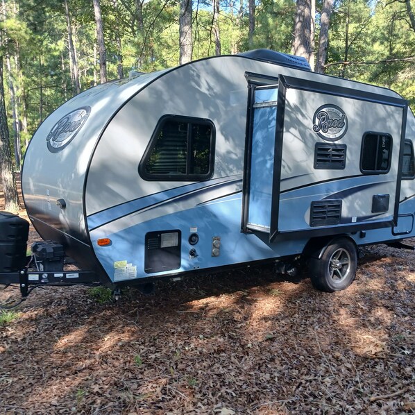 A silver RV with a side door, a small window, and a logo on the side. - Luxury Retreat RV with AC&Heat (Marston)