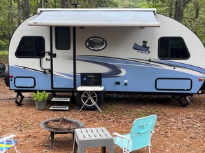 A recreational vehicle with a mounted television, a small table, a chair, and a fire pit.