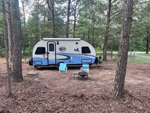 A recreational vehicle (RV) parked in a wooded area with two chairs and a table. - Luxury Retreat RV with AC&Heat (Marston)