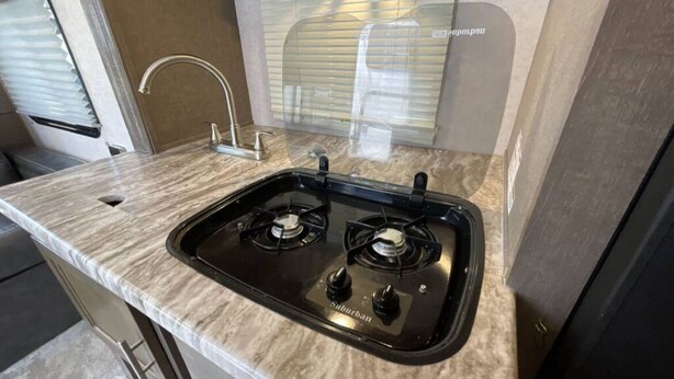 A kitchen with a gas stove, a sink, and a window with blinds.