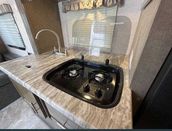 A kitchen with a gas stove, a sink, and a window with blinds. - Luxury Retreat RV with AC&Heat (Marston)