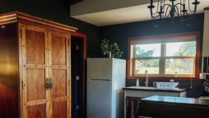 Una cocina con un armario de madera, un refrigerador blanco, una mesa de comedor con un florero y una ventana con vistas a árboles.