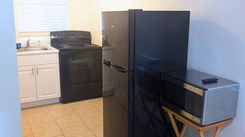 Une cuisine compacte avec un réfrigérateur noir, une cuisinière et un four à micro-ondes placés sur un meuble en bois.
