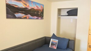 Een kamer met een bed, een kussen, een welkomstkaart, een landschapsafbeelding en een plank.