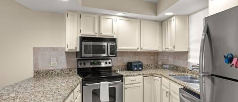 A kitchen with white cabinets, stainless steel appliances, a granite countertop, and a red rug.
