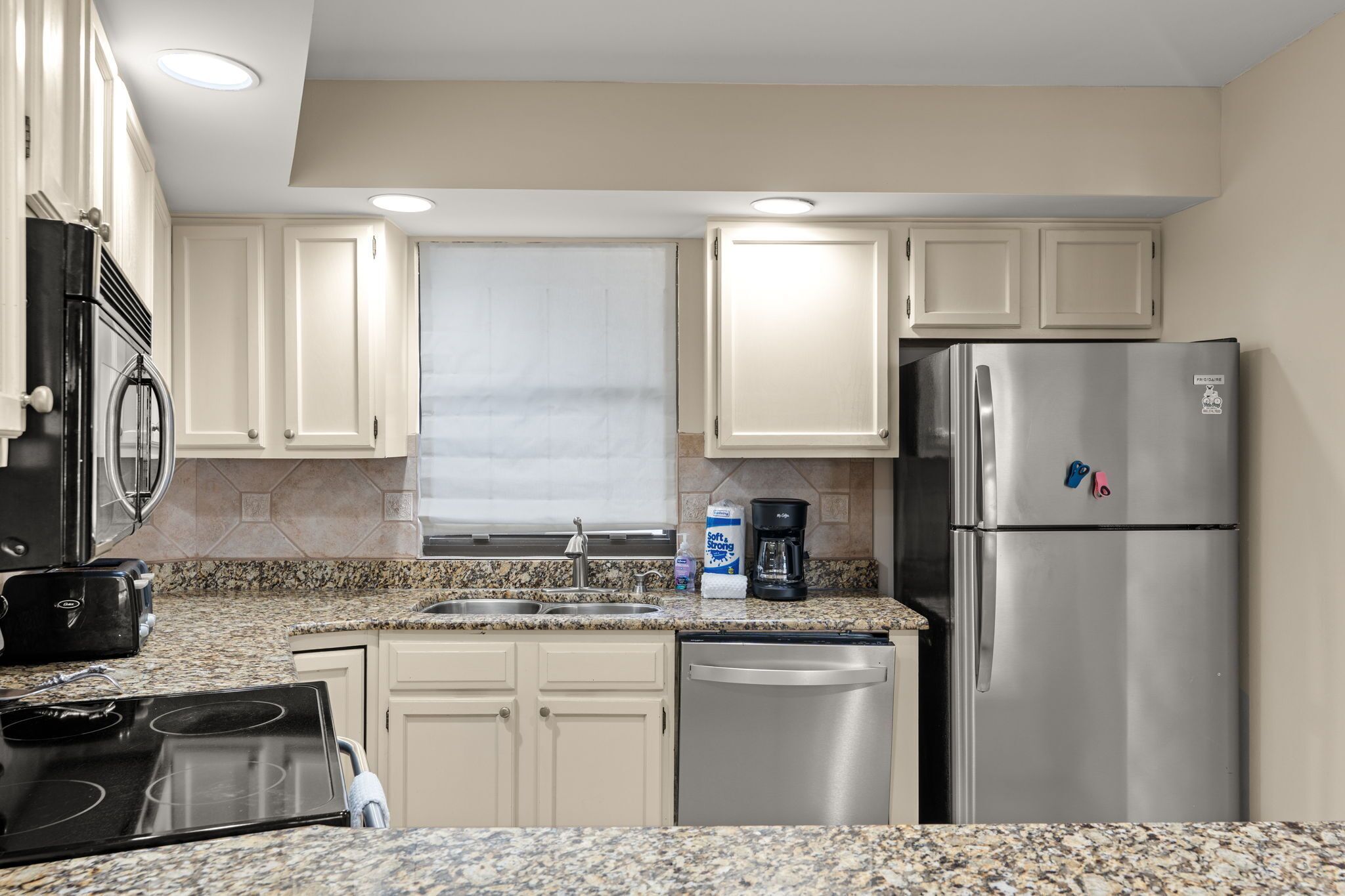 A kitchen with white cabinets, a stainless steel refrigerator, a stove, and a dishwasher.