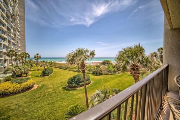 A balcony with a view of a well-maintained garden, palm trees, and a distant beach.