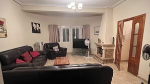 A living room with a black sofa, a wooden coffee table, a TV, and a fireplace. - Mediterranean villa with private pool 20 minutes from the beaches of La Marina (Catral)