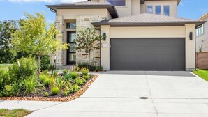 A modern two-story house with a stone facade, a large garage, and a landscaped front yard with various plants. - Dakota Cottage - Stay for 10 (New Braunfels)