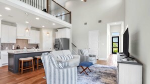 A spacious living area with a kitchen, a sofa, a coffee table, and a TV. - Dakota Cottage - Stay for 10 (New Braunfels)