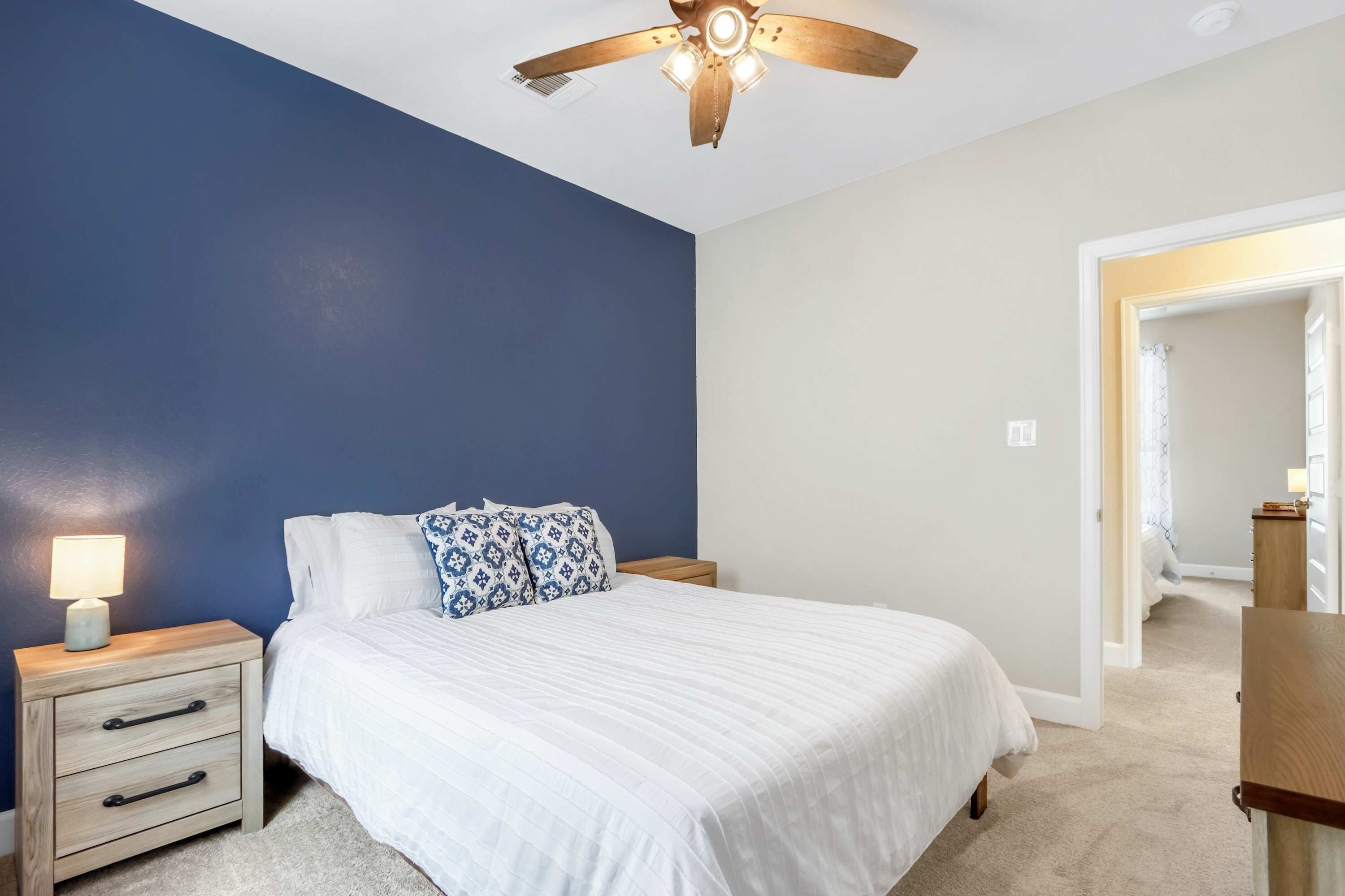A bedroom with a bed, nightstands, a ceiling fan, and a night lamp.