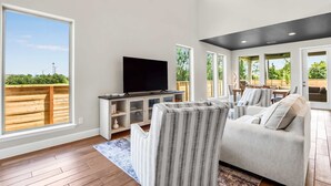 A spacious living room with a large TV, comfortable seating, and a view of the outdoors. - Dakota Cottage - Stay for 10 (New Braunfels)
