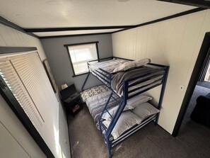 Ein Schlafraum mit Etagenbetten, einem Fenster, einem Schreibtisch und einer Heizung.