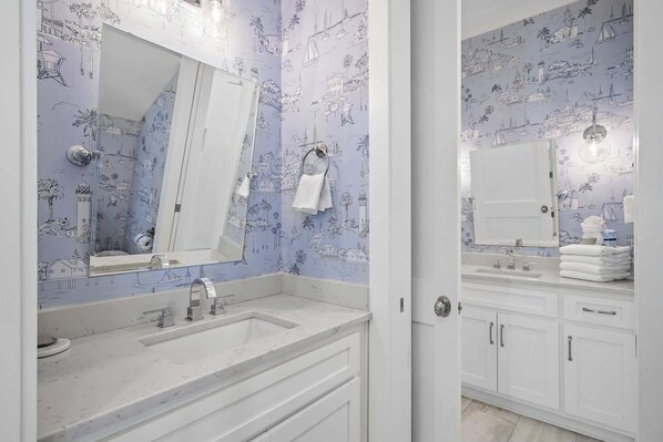 A bathroom with a white vanity, a large mirror, and a tiled wall with nautical illustrations.