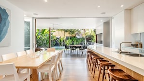 A modern kitchen with a large island, white cabinetry, and a view of a lush garden. - Lady Luxe (Byron Bay)
