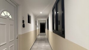 Un passadís llarg i estret amb parets blanques i beix, un sòl de rajoles i una porta al final.