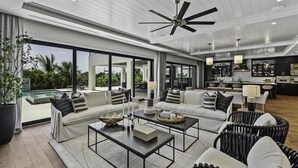 A spacious living area with a large sofa set, coffee table, and wicker chairs, featuring a view of a pool and outdoor patio.