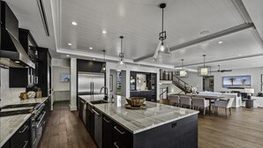 A modern kitchen with a large island, dark cabinetry, and stainless steel appliances.