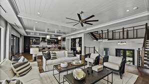 A spacious living room with a high ceiling, a central coffee table, sofas, and a staircase leading to an upper level.