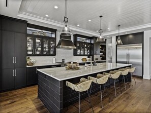 A modern kitchen with dark cabinetry, a large island, and bar stools. - 854 Grand Pass - Hill Tide - Sleeps 8 - Elevator - 14 night Minimum (Boca Grande)