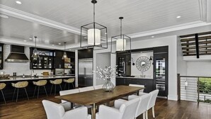 A modern kitchen with a central island, bar stools, and a dining table with white chairs.