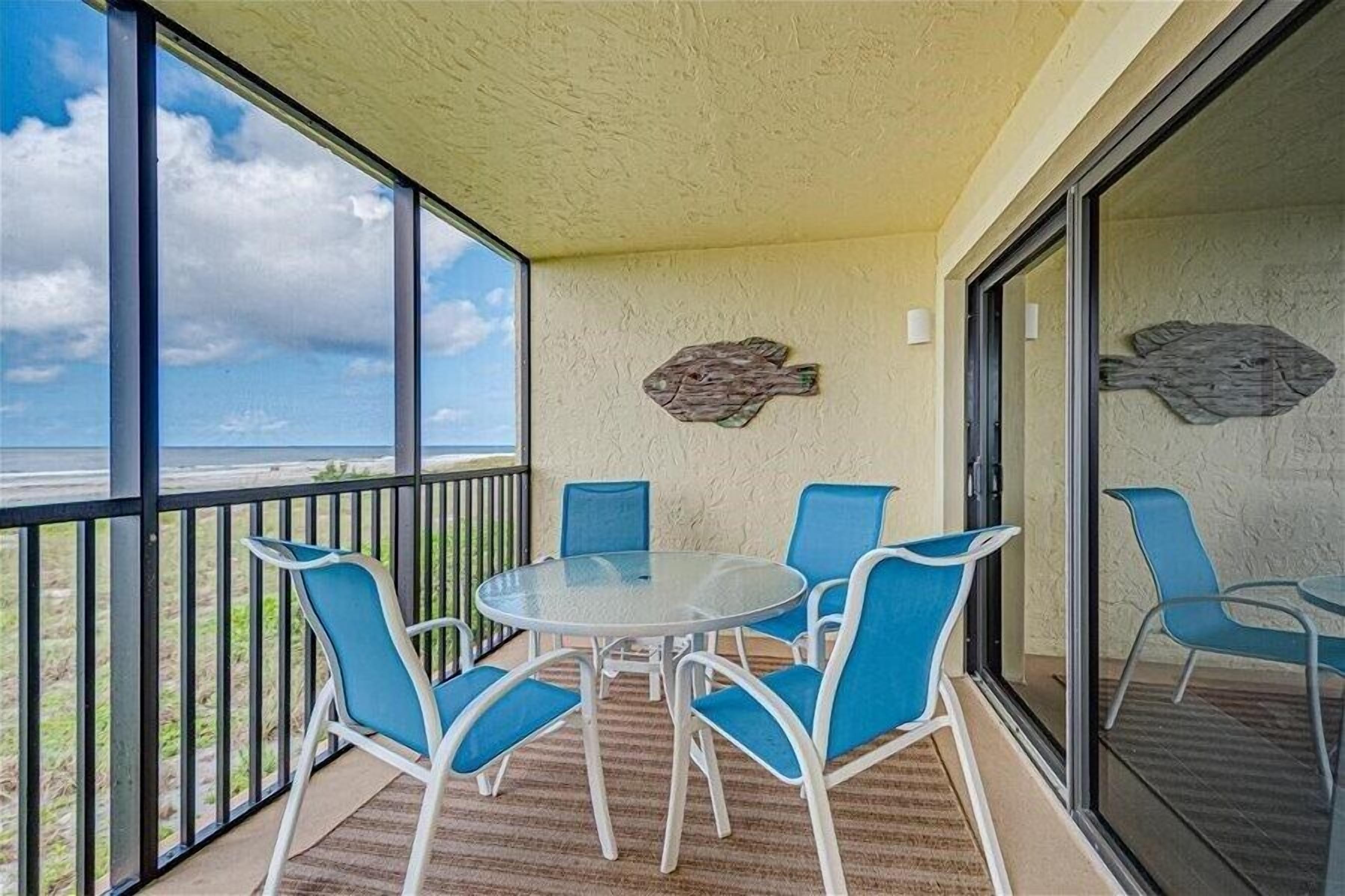 Ein Balkon mit Glastisch und blauen Stühlen, mit Blick auf einen Strand.