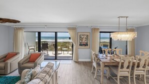 A spacious living room with a large glass door leading to a balcony overlooking the beach. There is a dining area with a wooden table and chairs. - Luxurious 2BR/2BA Gulf-front Boca Grande condo (Boca Grande)