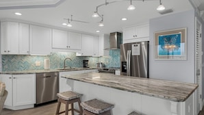 A modern kitchen with white cabinetry, a stainless steel refrigerator, and a herringbone-patterned backsplash. - Luxurious 2BR/2BA Gulf-front Boca Grande condo (Boca Grande)